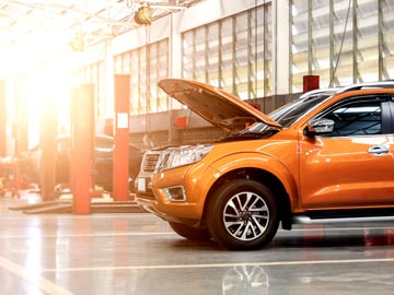 Ein orangefarbenes SUV steht in einer gut beleuchteten Auto-Werkstatt bei Autoankauf Ulm, dessen Motorhaube offen ist und den Motor zeigt.